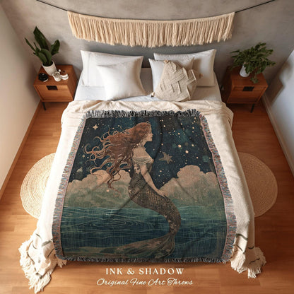 May include: A woven throw blanket featuring a mermaid illustration in shades of blue, green, and brown. The mermaid is depicted with long flowing hair and a fish tail, set against a starry night sky and ocean waves. The blanket has a fringed edge and the text "INK & SHADOW Original Fine Art Throws".