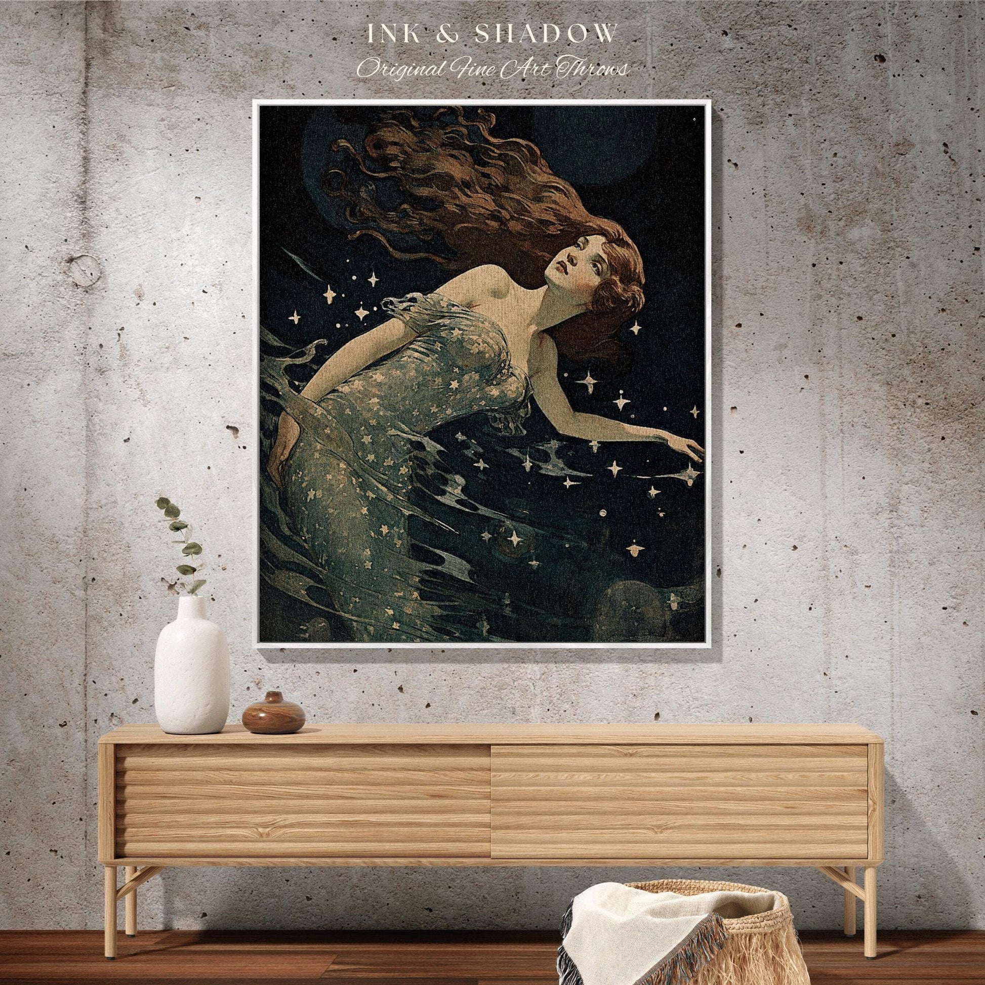 May include: A framed art print featuring a vintage illustration of a woman with long auburn hair, floating in dark water with stars. The artwork is titled "INK & SHADOW Original Fine Art Throws". The print is displayed above a wooden cabinet.