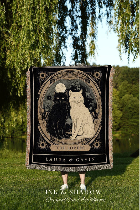 May include: Black and beige throw blanket featuring a circular design with two cats, one black and one white, under a full moon. The text "THE LOVERS" and names "LAURA & GAVIN" are below the image. The blanket has a fringed edge.