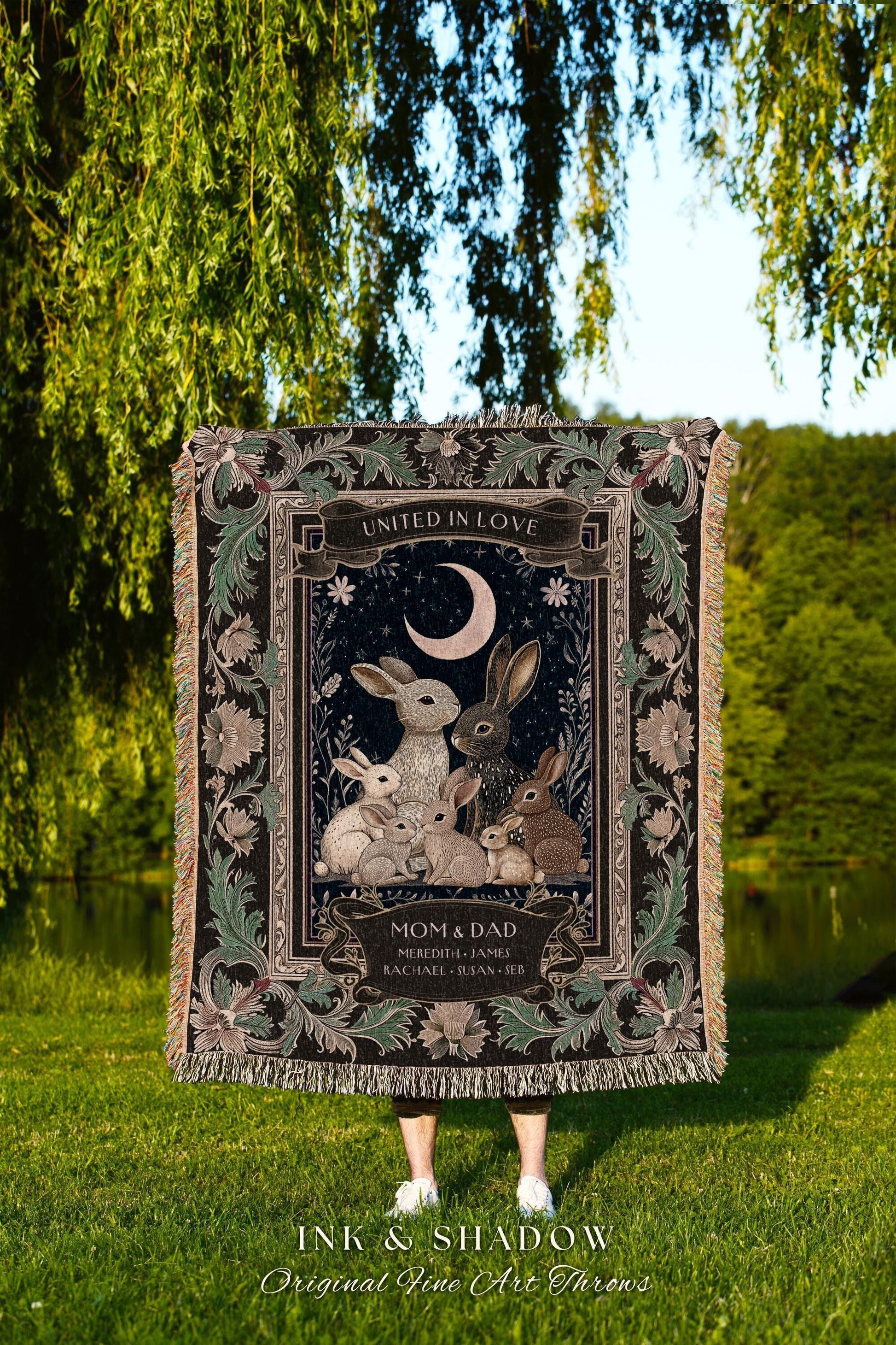 May include: A decorative throw blanket featuring a family of rabbits under a crescent moon, with the words "United in Love" at the top. The blanket has a dark background with floral accents and the text "Mom & Dad". The bottom reads "Ink & Shadow".