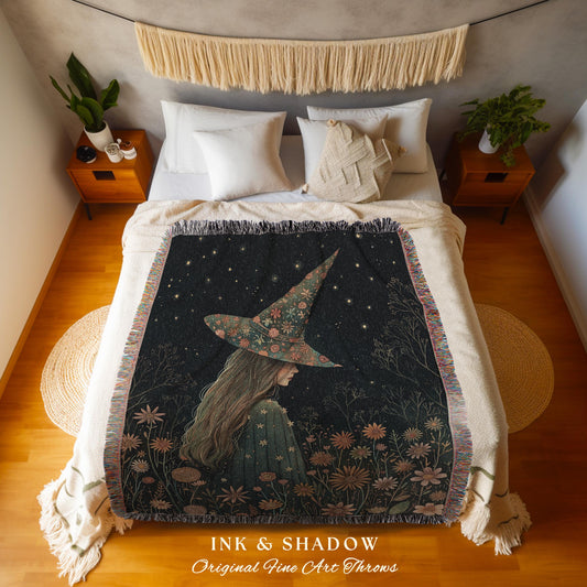 May include: A black throw blanket featuring a witch with a floral hat and a starry night sky design. The blanket has a fringed edge and the text "INK & SHADOW Original Fine Art Throws" at the bottom.