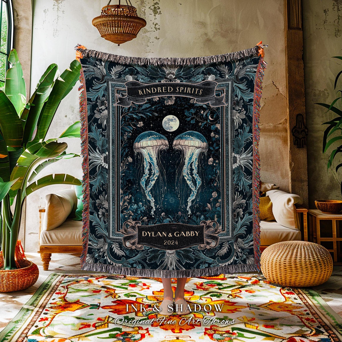 May include: A dark blue throw blanket featuring a design with two jellyfish, a full moon, and floral accents. The words "Kindred Spirits" and "Dylan & Gabby 2024" are displayed on the blanket. The blanket has a fringed edge.