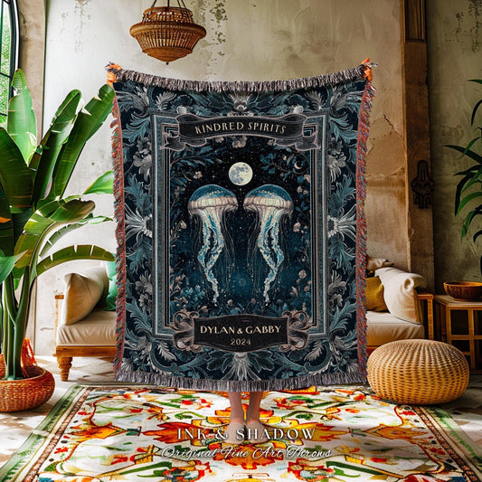 May include: A dark blue throw blanket featuring a design with two jellyfish, a full moon, and floral accents. The words "Kindred Spirits" and "Dylan & Gabby 2024" are displayed on the blanket. The blanket has a fringed edge.