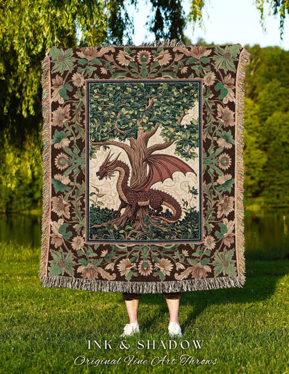 May include: A tapestry throw blanket featuring a dragon and tree design. The dragon is brown with red wings, and the tree has green leaves. The border is brown with floral and leaf patterns. The blanket has a fringed edge. The text "INK & SHADOW Original Fine Art Throws" is at the bottom.