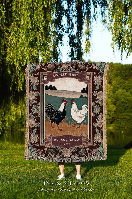 May include: A woven throw blanket featuring a framed illustration of two roosters, one black and one white, against a landscape backdrop. The blanket has a dark brown border with floral accents and the text "KINDRED SPIRITS" and "DYLAN & GABBY 2024". The bottom reads "INK & SHADOW Original Fine Art Throws".