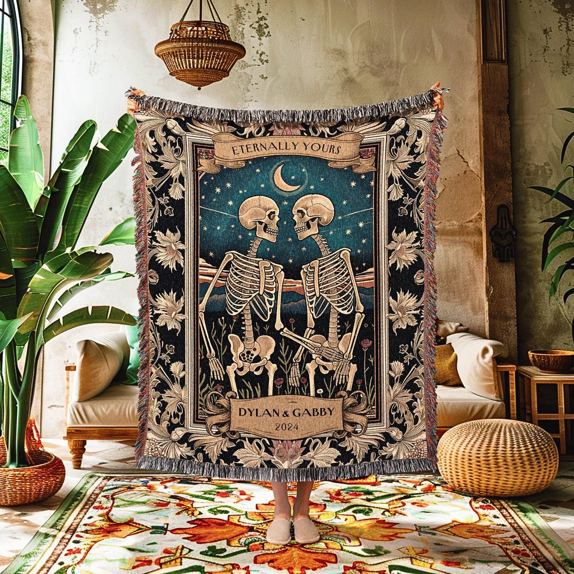 May include: A woven tapestry blanket featuring a romantic scene with two skeletons facing each other under a starry night sky. The blanket has a dark blue background with the words "Eternally Yours" and "Dylan & Gabby 2024". The edges are fringed.