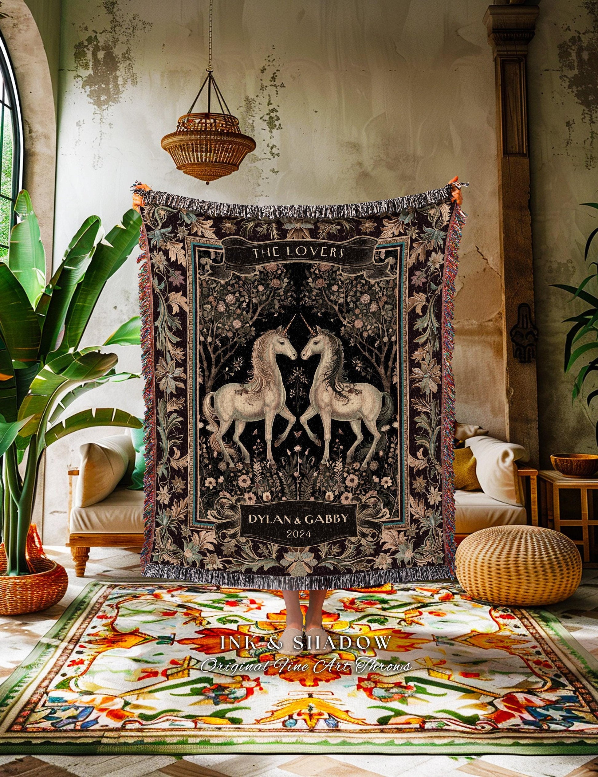 May include: A tapestry throw blanket featuring two white unicorns facing each other against a black background. The blanket has a decorative border and the words "THE LOVERS" and "DYLAN & GABBY 2024" are printed on it. The blanket has fringed edges.
