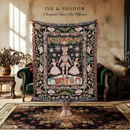 May include: A black throw blanket with a detailed illustration of a Nutcracker, two dancers, and wrapped gifts. The blanket has a floral border with pink and green accents. The text "INK & SHADOW Original Fine Art Throws" is at the top.