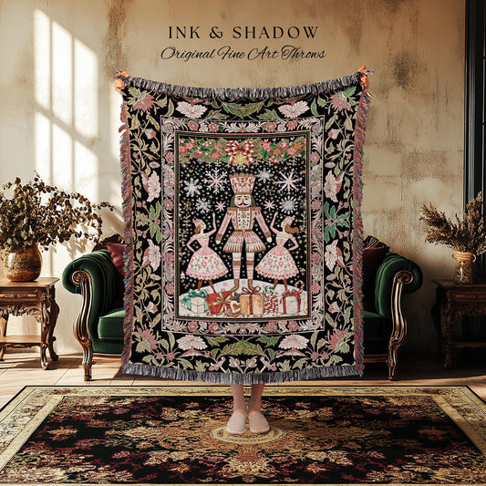 May include: A black throw blanket with a detailed illustration of a Nutcracker, two dancers, and wrapped gifts. The blanket has a floral border with pink and green accents. The text "INK & SHADOW Original Fine Art Throws" is at the top.
