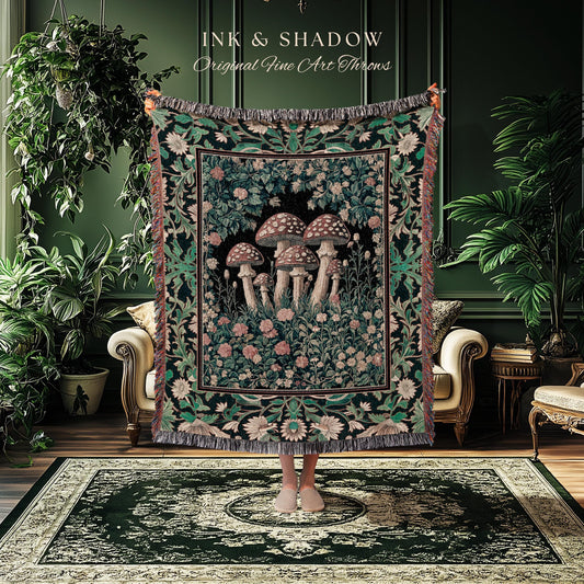 May include: A woven throw blanket featuring a mushroom design. The blanket has a black background with a border of green and cream floral patterns. The center of the blanket displays a cluster of mushrooms with pink and cream flowers.