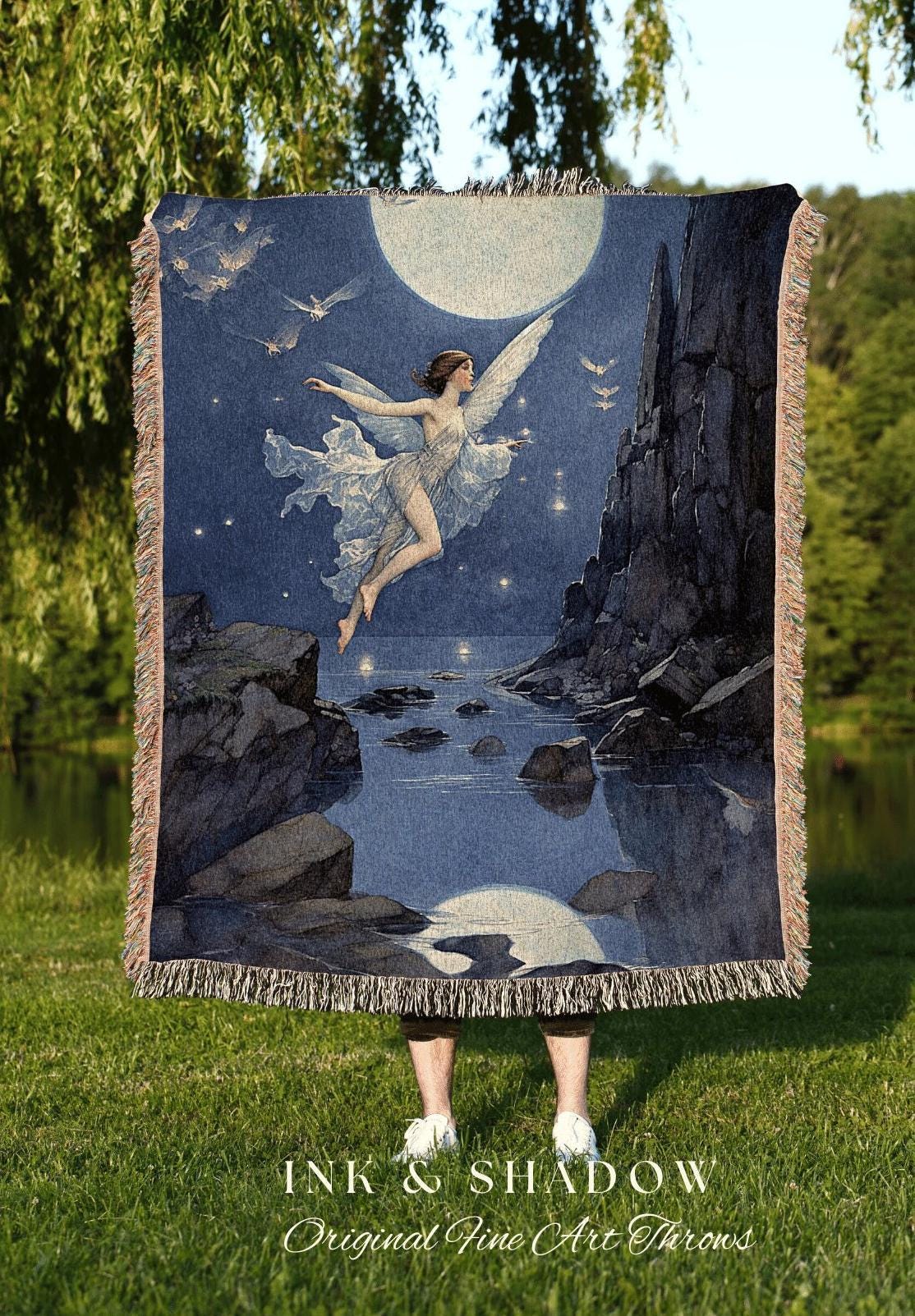 May include: A woven throw blanket featuring a celestial scene with a winged figure, a full moon, and flying birds. The artwork is in shades of blue, gray, and white, with a fringed edge. The text "INK & SHADOW Original Fine Art Throws" is at the bottom.