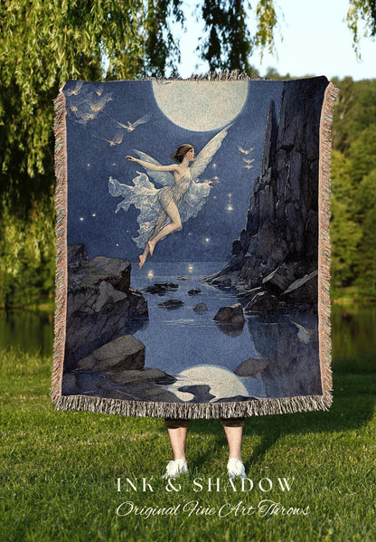 May include: A woven throw blanket featuring a celestial scene with a winged figure, a full moon, and flying birds. The artwork is in shades of blue, gray, and white, with a fringed edge. The text "INK & SHADOW Original Fine Art Throws" is at the bottom.
