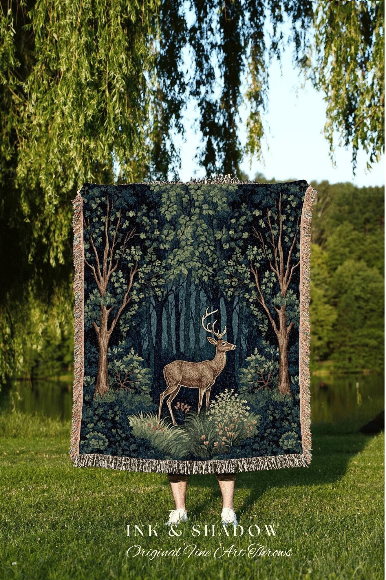 May include: A dark blue and green tapestry throw blanket featuring a forest scene with a deer. The blanket has a fringed edge and the text "INK & SHADOW Original Fine Art Throws".
