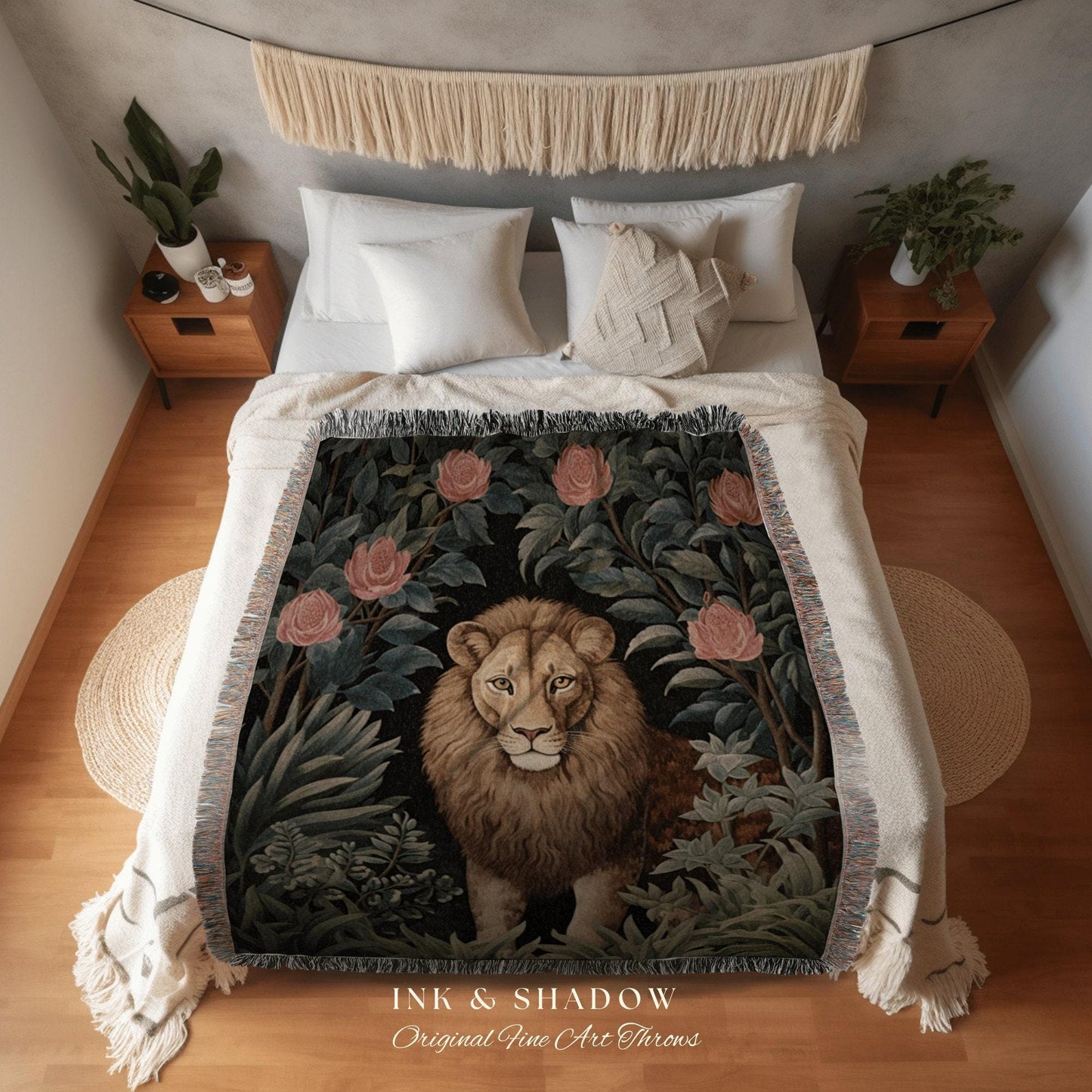 May include: A woven throw blanket featuring a lion surrounded by roses and foliage. The design is set against a black background, with the text "INK & SHADOW Original Fine Art Throws" at the bottom. The blanket is draped over a bed with white bedding.