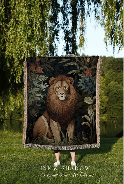 May include: A decorative throw blanket featuring a detailed illustration of a lion in a jungle setting. The lion is brown and tan, surrounded by green foliage and flowers. The blanket has a fringed edge and the text "INK & SHADOW Original Fine Art Throws".