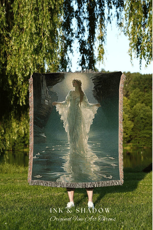 May include: A woven throw blanket featuring a serene image of a woman in a flowing white gown standing in water. The artwork has a soft, ethereal quality with a muted color palette. The blanket has a fringed edge and the text "INK & SHADOW Original Fine Art Throws".