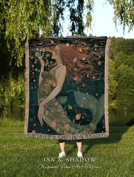 May include: A woven throw blanket featuring a mermaid illustration in shades of teal, green, and gold. The mermaid has long flowing red hair and is surrounded by bubbles. The blanket has a fringed edge and the text "INK & SHADOW Original Fine Art Throws".