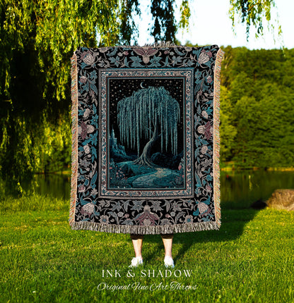 May include: A woven tapestry throw blanket with a black background and a detailed floral border. The center of the blanket features a dark blue willow tree with a crescent moon above it. The tree is surrounded by a dark blue path and a castle in the distance. The text 'INK & SHADOW Original Fine Art Throws' is printed below the blanket.