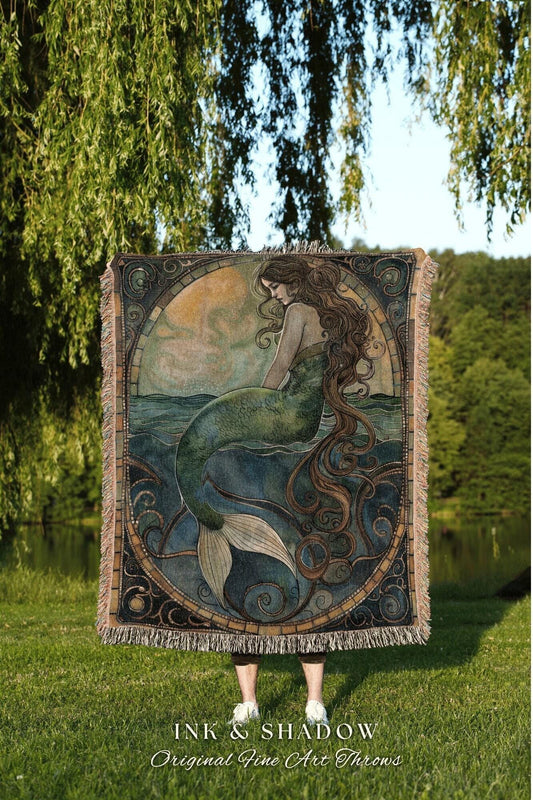 May include: A woven throw blanket featuring a mermaid illustration. The artwork depicts a mermaid with long brown hair and a green tail, seated in the ocean. The blanket has a fringed edge and the text "INK & SHADOW Original Fine Art Throws".