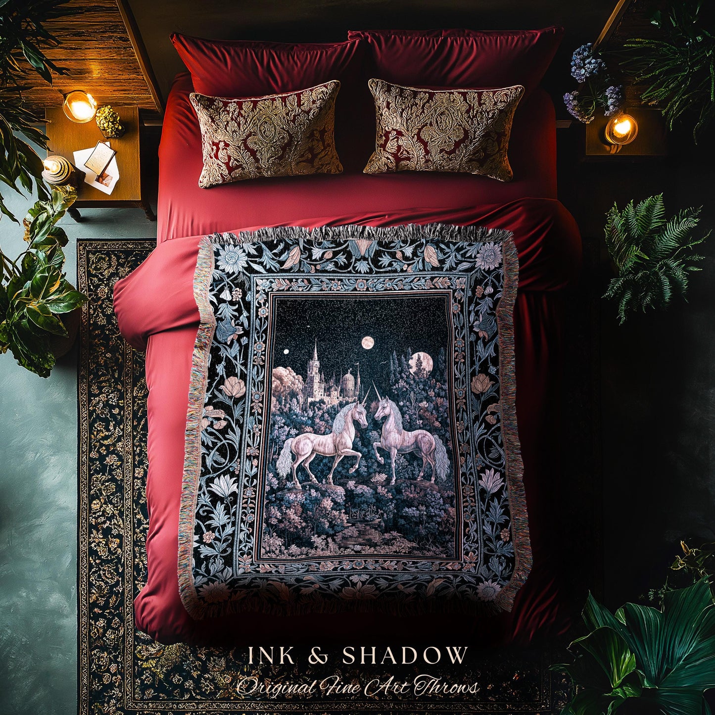 May include: A decorative throw blanket featuring a nighttime scene with two unicorns, a castle, and a full moon. The blanket is black with a floral border and the text "INK & SHADOW Original Fine Art Throws". The blanket is on a red bed with matching pillows.