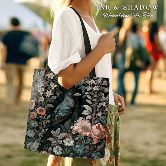May include: A black tote bag with a woven design featuring a dark blue bird perched on a branch with pink and white flowers. The bag has the text "INK & SHADOW Woven Fine Art Tote" printed on the top.
