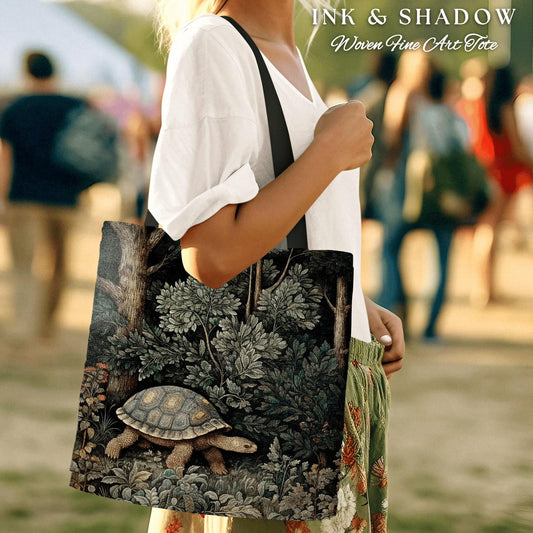 May include: A black tote bag with a woven design featuring a turtle walking through a forest. The bag has the text "INK & SHADOW Woven Fine Art Tote" printed on the top.