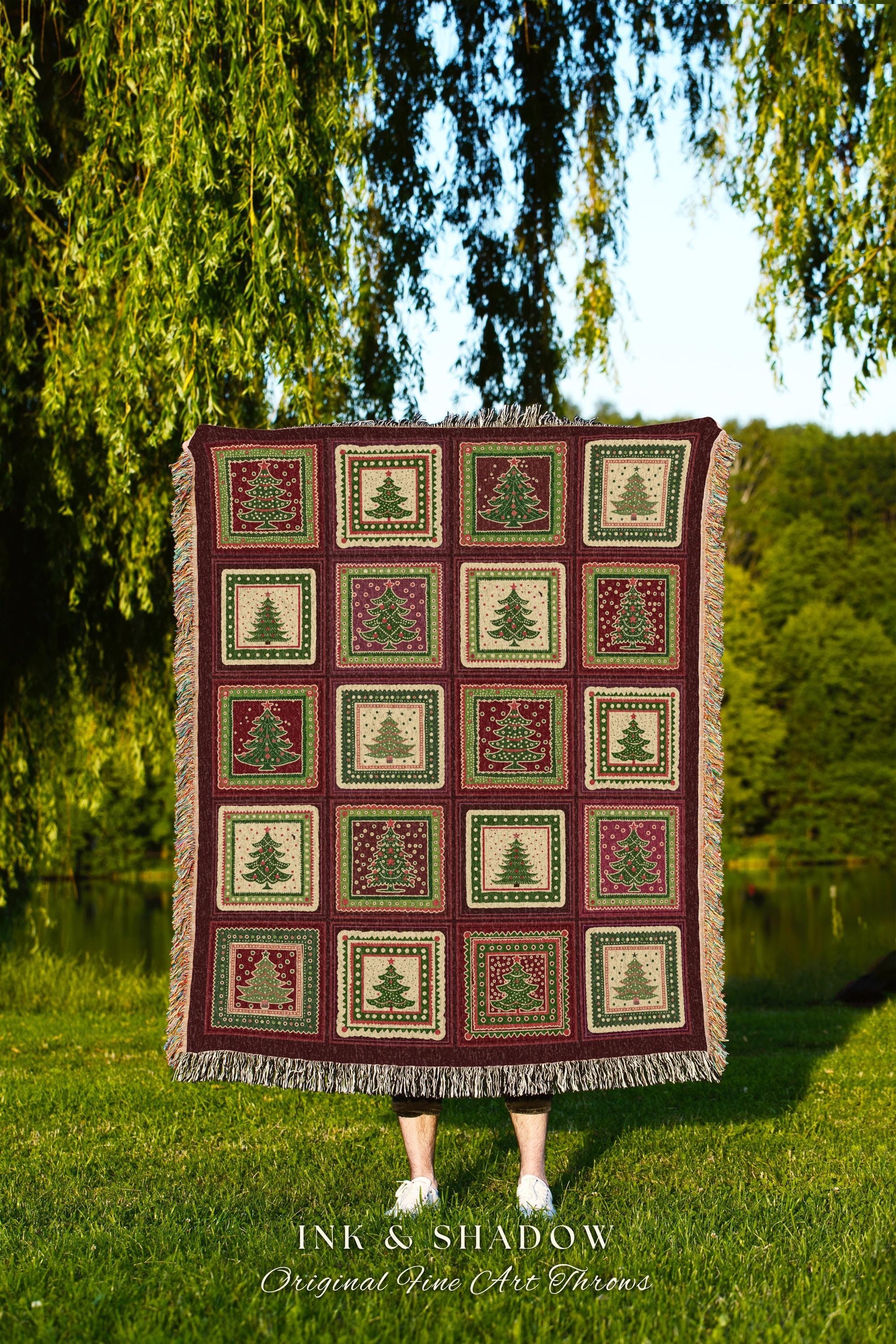 May include: A burgundy throw blanket with a repeating pattern of Christmas trees in squares. The trees are green and red, set against a cream and burgundy background. The blanket has a fringed edge and the text "INK & SHADOW Original Fine Art Throws".
