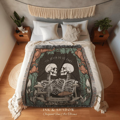 May include: A decorative throw blanket featuring a skeletal couple embracing, with the text "TIL DEATH DO US PART." The design includes floral and botanical elements in shades of green, brown, and orange. The blanket is displayed on a bed with white bedding.
