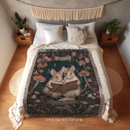 May include: A woven throw blanket featuring an illustration of two mice reading a book, surrounded by mushrooms and flowers. The blanket has a dark teal background with the words "Kindred Spirits" and "London & Dakota" printed on it. The words "INK & SHADOW Original Fine Art Throws" are printed at the bottom.