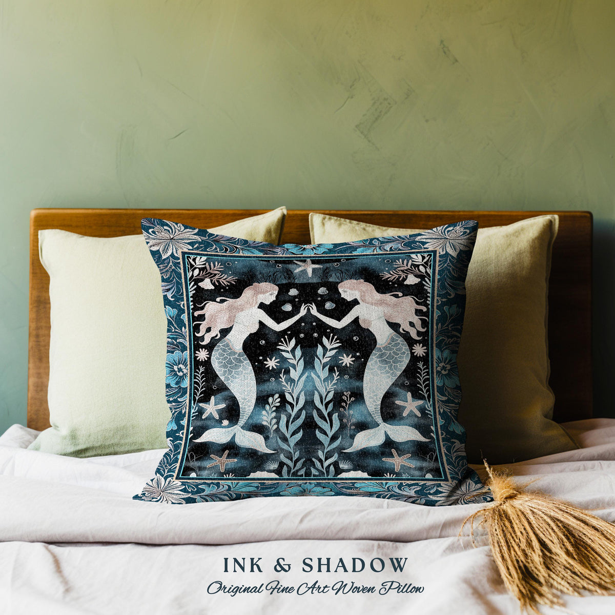 May include: A blue and white woven pillow featuring a design of two mermaids with flowing tails, surrounded by seaweed and stars. The pillow has a dark blue background and a border of floral patterns. The text "INK & SHADOW Original Fine Art Woven Pillow" is printed below the pillow.