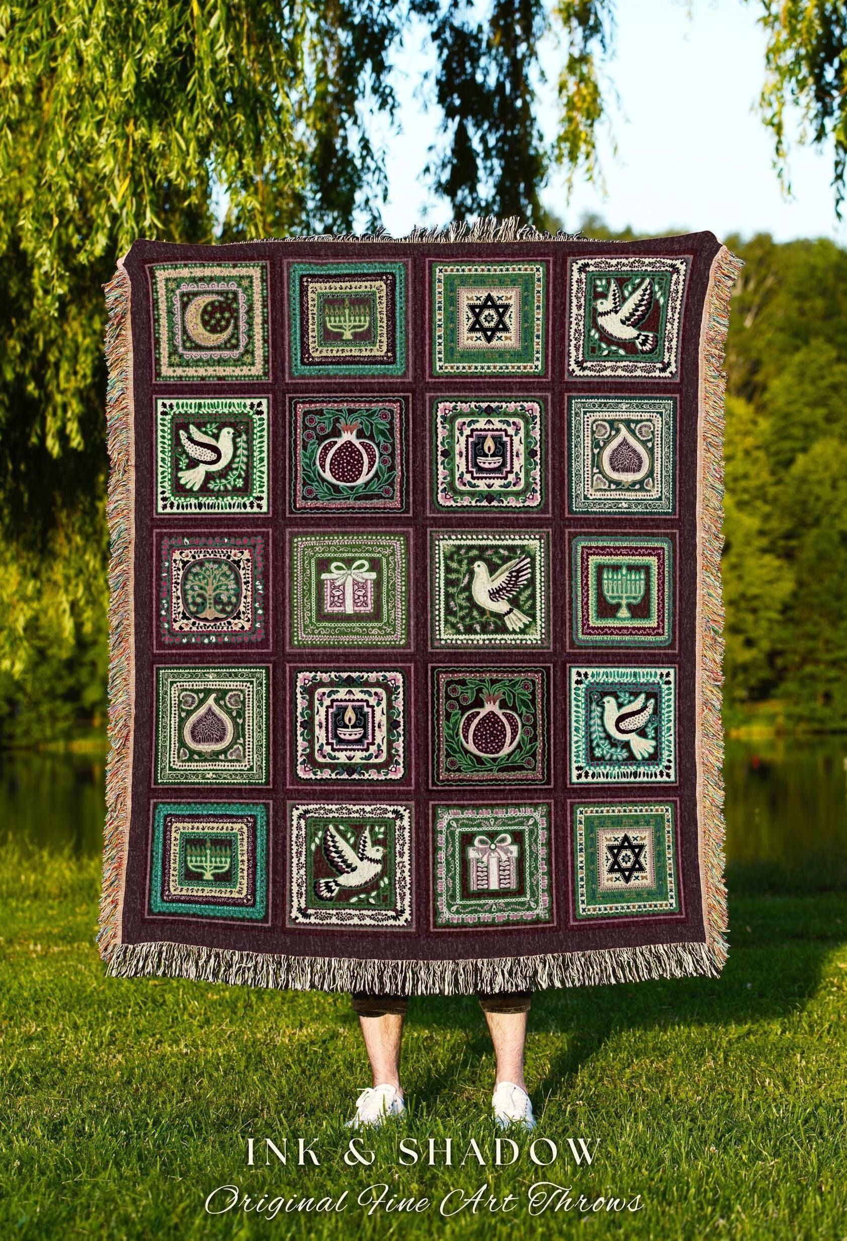 May include: A woven throw blanket with a repeating pattern of square panels. Each panel features a different design, including a dove, pomegranate, and Star of David, in shades of green, white, and burgundy. The blanket has a fringed edge and the text "INK & SHADOW Original Fine Art Throws".