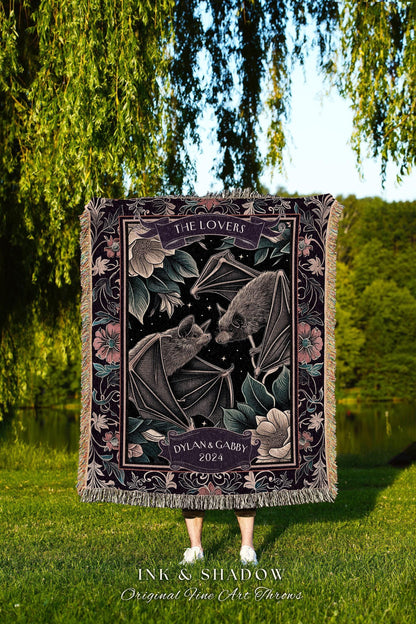 May include: A woven throw blanket with a dark background featuring two bats, flowers, and the text "THE LOVERS" and "DYLAN & GABBY 2024." The blanket has a fringed edge and the words "INK & SHADOW Original Fine Art Throws" are at the bottom.