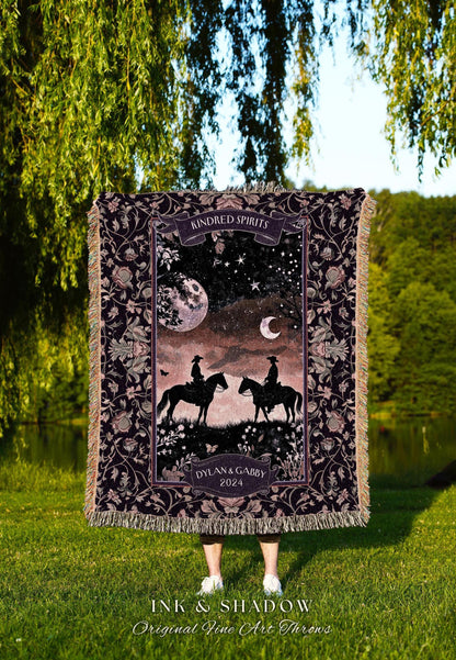 May include: A decorative throw blanket with a dark floral pattern and fringe. The center features a night scene with two riders on horseback, a moon, and stars. Text includes "Kindred Spirits" and "Dylan & Gabby 2024". The blanket is displayed outdoors.