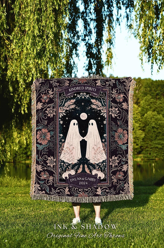 May include: A dark-colored throw blanket with a floral and ghost design. The blanket features the text "Kindred Spirits" and "Dylan & Gabby 2024". The bottom of the blanket has a fringe. The words "Ink & Shadow" are at the bottom.