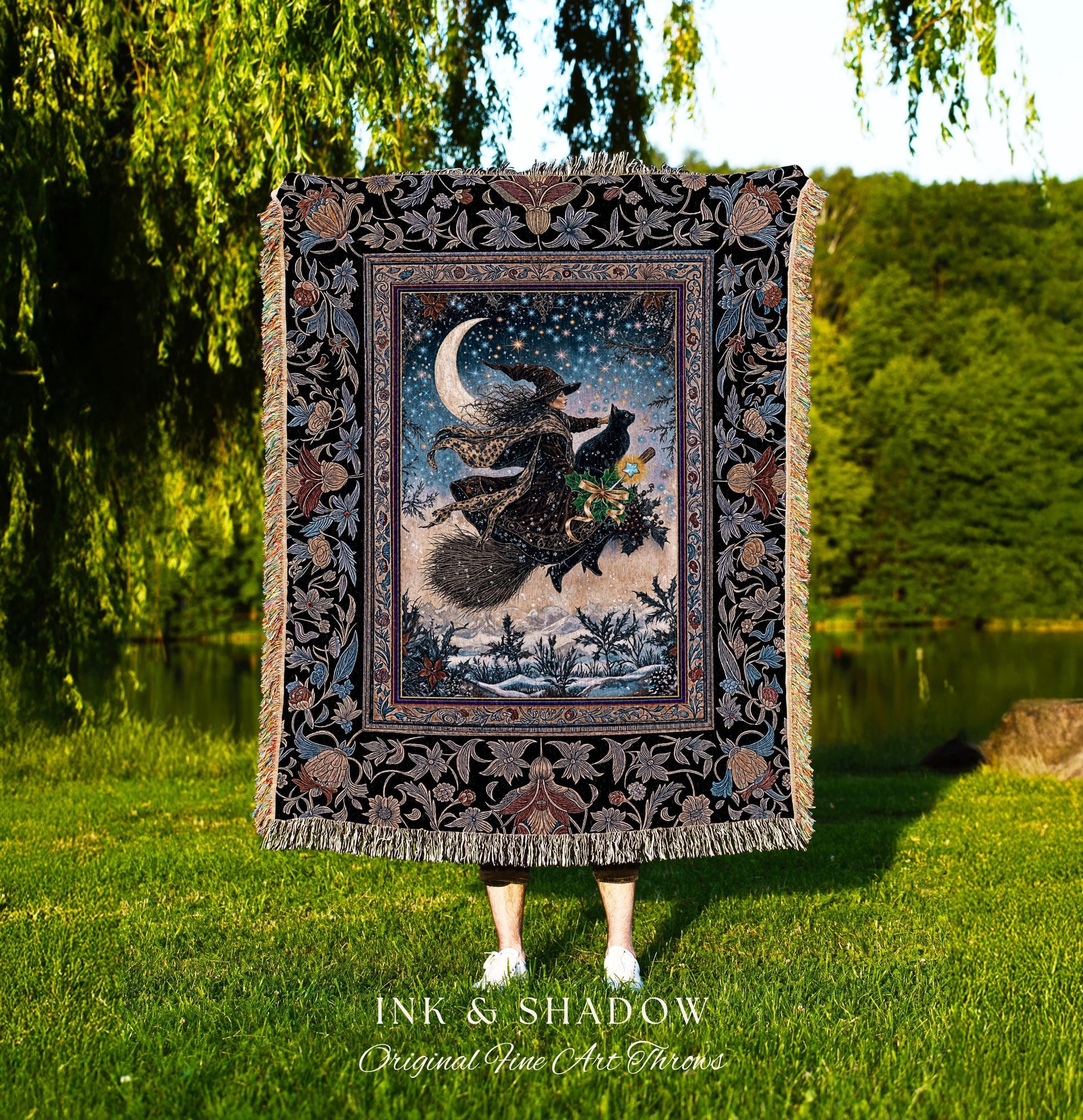 May include: A decorative throw blanket featuring a witch flying on a broomstick with a black cat under a crescent moon and starry sky. The blanket has a black floral border and fringe. The text "INK & SHADOW Original Fine Art Throws" is at the bottom.