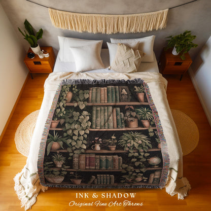 May include: A black throw blanket featuring a bookshelf design with books and potted plants. The blanket has a fringed edge and the text "INK & SHADOW Original Fine Art Throws" at the bottom.