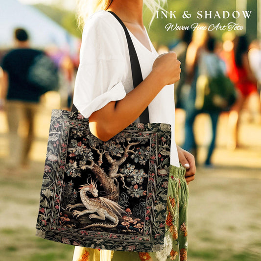 May include: A black tote bag with a woven tapestry design featuring a white dragon curled around a tree. The tapestry is surrounded by a black border with floral details. The text "INK & SHADOW Woven Fine Art Tote" is printed on the bag.