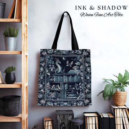 May include: A blue and white tote bag with a woven design featuring a dragon, books, and a moon. The text "INK & SHADOW Woven Fine Art Tote" is printed on the bag.
