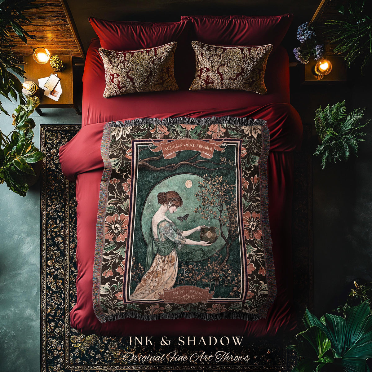 May include: A decorative throw blanket with a vintage art print featuring a woman in a garden scene. The blanket has a dark border with floral patterns and the text "INK & SHADOW Original Fine Art Throws". The bed has red bedding and decorative pillows.