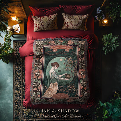 May include: A decorative throw blanket with a vintage art print featuring a woman in a garden scene. The blanket has a dark border with floral patterns and the text "INK & SHADOW Original Fine Art Throws". The bed has red bedding and decorative pillows.