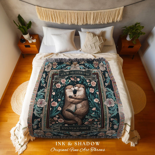 May include: A dark green throw blanket with a floral and otter design. The blanket features the text "YOU'RE MY OTTER HALF" and "DYLAN & GABBY 2024". The blanket is fringed and has a decorative border with pink and teal accents. The words "INK & SHADOW Original Fine Art Throws" are at the bottom.