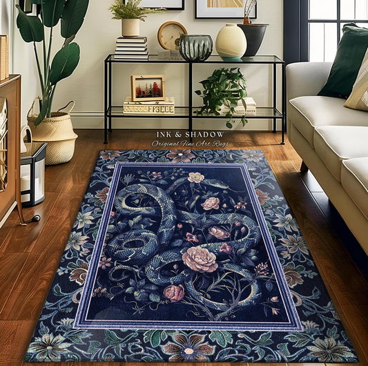 May include: A dark blue rug featuring a central design of intertwined snakes and roses. The rug has a floral border and a rectangular inner frame. The text "INK & SHADOW Original Fine Art Rugs" is visible in the upper right corner.