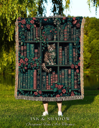 May include: A decorative throw blanket featuring a bookshelf design with a cat. The blanket has a dark background with images of books, flowers, and a cat. The text "INK & SHADOW Original Fine Art Throws" is at the bottom.