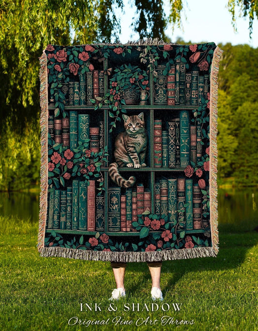May include: A decorative throw blanket featuring a bookshelf design with a cat. The blanket has a dark background with images of books, flowers, and a cat. The text "INK & SHADOW Original Fine Art Throws" is at the bottom.