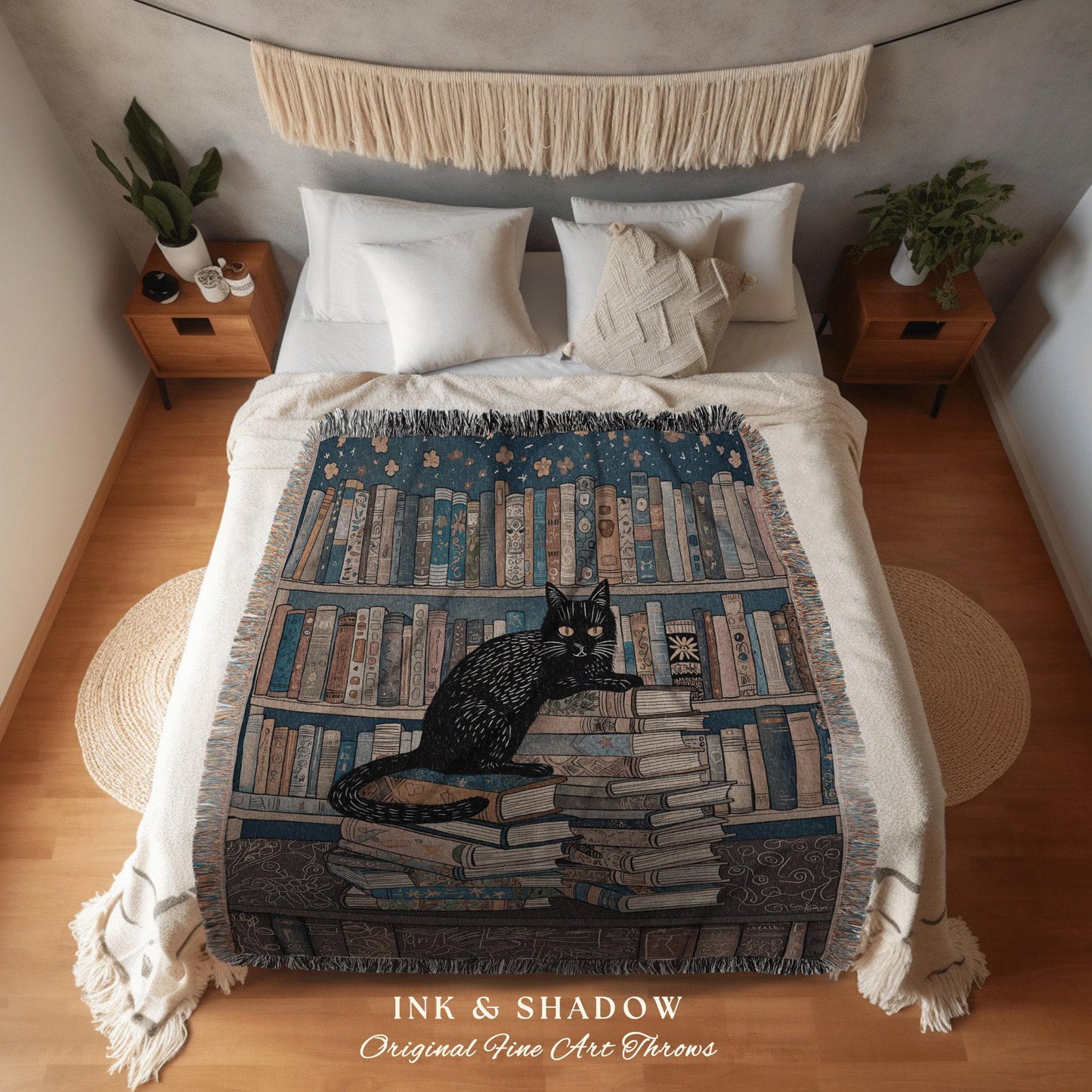 May include: A woven throw blanket featuring a black cat perched on a stack of books in front of a bookshelf design. The blanket has a blue and cream color scheme with the text "INK & SHADOW Original Fine Art Throws".