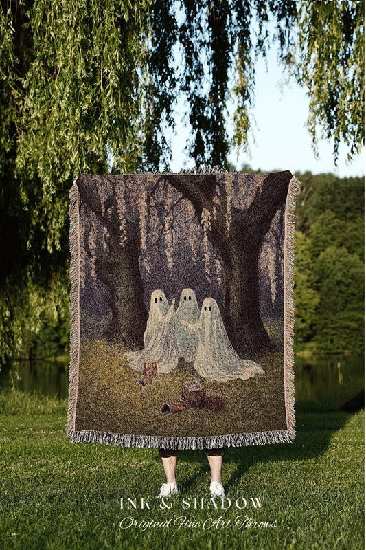 May include: A woven throw blanket featuring a spooky forest scene with three friendly ghosts. The blanket has a fringed edge and the text "INK & SHADOW Original Fine Art Throws" at the bottom. The color palette includes greens, browns, and off-white.