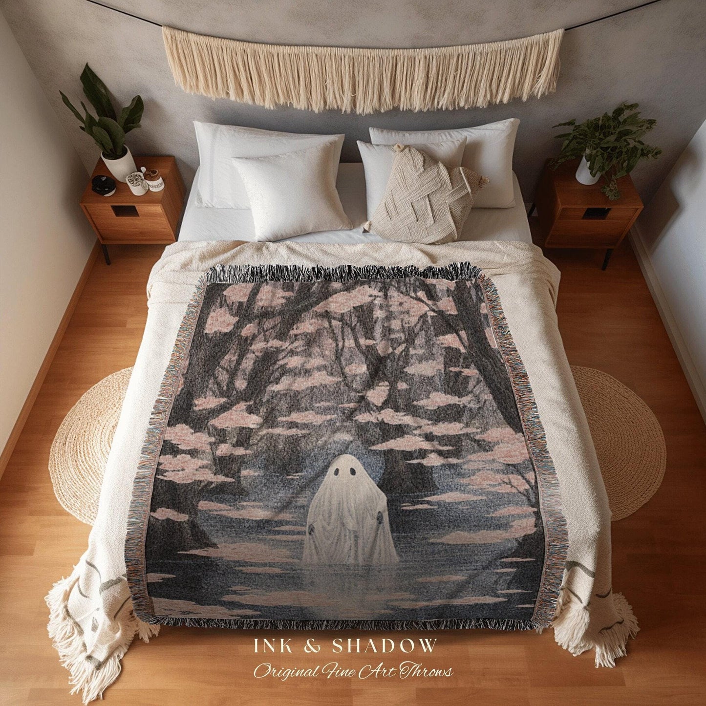 May include: A woven throw blanket featuring a spooky ghost in a misty forest scene. The blanket has a black, gray, and pink color palette with a fringed edge. The text "INK & SHADOW Original Fine Art Throws" is printed at the bottom.