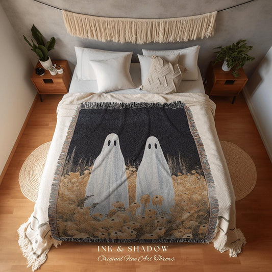 May include: A woven throw blanket featuring two white ghost figures against a dark background with a field of flowers. The blanket has a fringed edge and the text "INK & SHADOW Original Fine Art Throws".