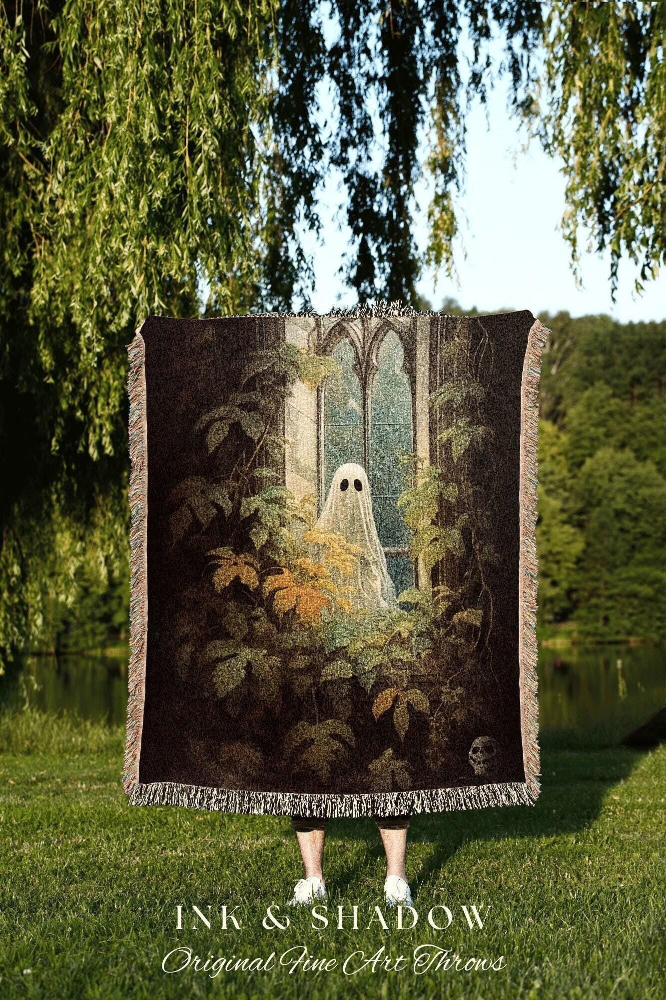 May include: A dark woven throw blanket featuring a ghost in a window surrounded by foliage. The throw has a fringed edge and the text "INK & SHADOW Original Fine Art Throws" at the bottom.