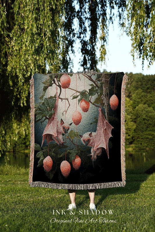 May include: A woven tapestry throw blanket with a dark background featuring a pink and green tree with pink bats hanging from the branches. The bats are holding onto pink fruit. The throw blanket has a black fringe border and the words 'INK & SHADOW Original Fine Art Throws' are printed at the bottom.